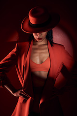 Image showing Woman, fashion hat and spotlight for suit, sexy and mystery in studio for beauty, punk aesthetic and cosmetics. Fashion model girl, cyberpunk design or unique with dark cosmetic by red background