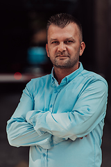 Image showing A successful young businessman in a shirt, with crossed arms, poses outdoors, confident expression on his face.