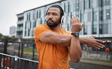 Image showing Fitness, runner or black man stretching in city for running training, cardio exercise or workout start in London. Wellness, mindset or healthy sports athlete in headphones streaming radio or podcast