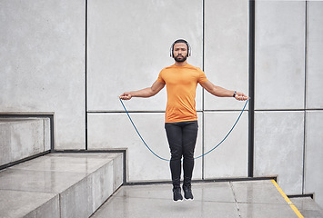 Image showing Fitness, skipping rope and man jump in city for wellness exercise, cardio workout and training with headphones. Sports, energy and athlete jumping with gym equipment, listening to music in urban town