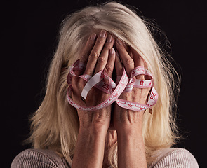 Image showing Hands, tape measure and anorexia with a woman holding her face in studio on a dark background in grief. Depression, eating disorder and bulimia with a female suffering with unhealthy weight loss