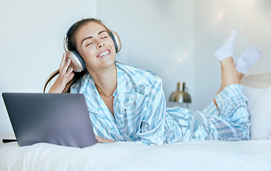 Image showing Headphones, laptop and woman on her bed with music for mental health, relax and wellness in morning sunshine or lens flare. Happy woman or student on internet, audio streaming subscription in bedroom