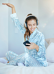 Image showing Headphones, phone and woman in bed dancing while listening to music, playlist or radio at her home. Happy, smile and young lady from Canada in pajamas streaming audio, album or song with a cellphone.