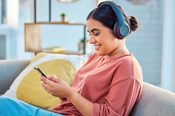 Image showing Indian woman, music headphones and smartphone in living room for social media app, radio podcast and ebook listening on sofa. Young girl, mobile audio streaming and watch web with technology at home