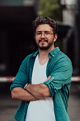 Image showing A successful young businessman in a shirt, with crossed arms, poses outdoors, confident expression on his face.