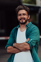 Image showing A successful young businessman in a shirt, with crossed arms, poses outdoors, confident expression on his face.