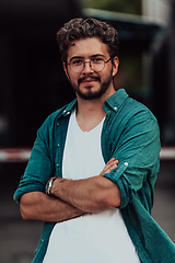 Image showing A successful young businessman in a shirt, with crossed arms, poses outdoors, confident expression on his face.