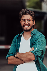 Image showing A successful young businessman in a shirt, with crossed arms, poses outdoors, confident expression on his face.