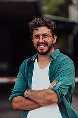 Image showing A successful young businessman in a shirt, with crossed arms, poses outdoors, confident expression on his face.