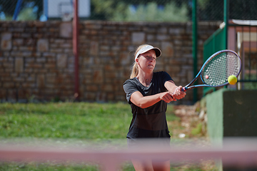 Image showing A young girl showing professional tennis skills in a competitive match on a sunny day, surrounded by the modern aesthetics of a tennis court.