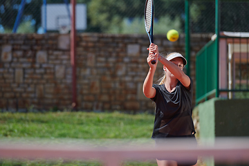 Image showing A young girl showing professional tennis skills in a competitive match on a sunny day, surrounded by the modern aesthetics of a tennis court.