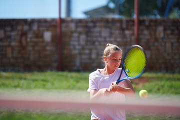 Image showing A young girl showing professional tennis skills in a competitive match on a sunny day, surrounded by the modern aesthetics of a tennis court.