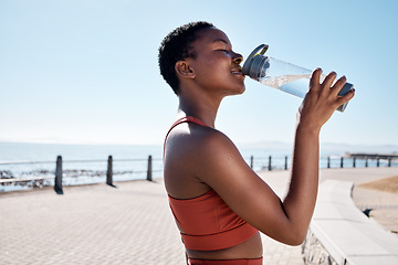 Image showing Black woman, drinking water or bottle in fitness workout, training or exercise by beach, ocean or sea in summer location. Smile, happy or sports runner with drink for healthcare wellness recovery