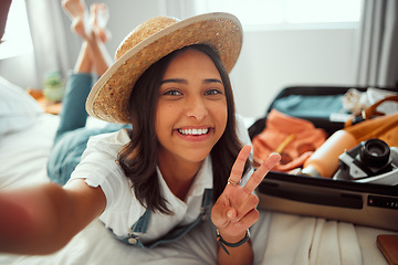 Image showing Portrait, travel and selfie by woman on bed with luggage, smile and happy before leaving for vacation. Face, girl and peaceful hand sign by travelling influencer pose for blog, photo and social media