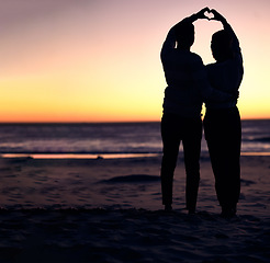 Image showing Couple, sunset silhouette and beach with heart sign hands, bonding and love on vacation for honeymoon. Man, woman and romantic hand signal by ocean with dusk sunshine for romance together in nature