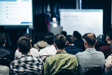 Image showing Speaker giving a talk in conference hall at business event. Rear view of unrecognizable people in audience at the conference hall. Business and entrepreneurship concept.