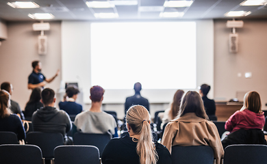 Image showing Speaker giving a talk in conference hall at business event. Rear view of unrecognizable people in audience at the conference hall. Business and entrepreneurship concept.