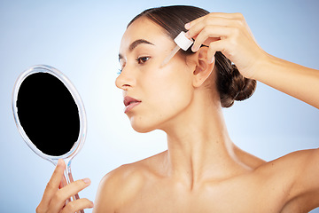 Image showing Face, skincare serum and woman with mirror in studio on a blue background. Beauty, cosmetics and female model with hyaluronic acid, essential oil and dropper product for healthy skin or anti aging.