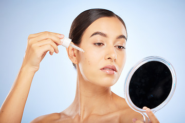 Image showing Face, skincare serum and woman with mirror in studio on a blue background. Beauty, cosmetics and female model with hyaluronic acid, essential oil and dropper product for healthy skin or anti aging.
