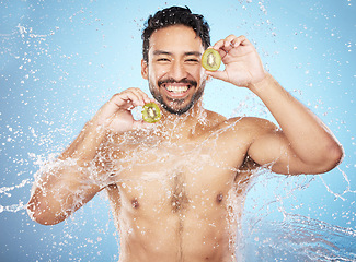 Image showing Face portrait, water splash and man with kiwi in studio isolated on a blue background. Cleaning, skincare and hygiene of happy male model washing fresh fruit for vitamin c, nutrition and healthy diet