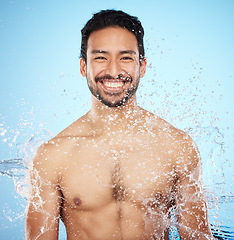 Image showing Portrait, water and shower with a man model in studio on a blue background for hygiene or hydration. Face, beauty and skincare with a handsome young male wet from a water splash in the bathroom