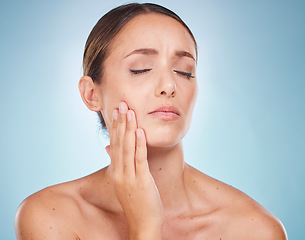 Image showing Toothache, dental hygiene and oral care with a model woman holding her face in pain on a blue background. Dentist, cavity and mouth with an attractive young female touching her cheek in studio