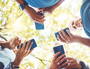 Image showing Fitness, group with smartphone in hands and running in park, technology low angle and check exercise mobile app. Elderly runner team outdoor with health, phone for cardio and sports motivation.