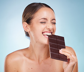 Image showing Skincare, beauty and woman with chocolate in a studio for a health, wellness and facial treatment. Cosmetics, diet and girl model eating sweet cacao candy while doing skin routine by blue background.