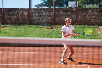 Image showing A young girl showing professional tennis skills in a competitive match on a sunny day, surrounded by the modern aesthetics of a tennis court.