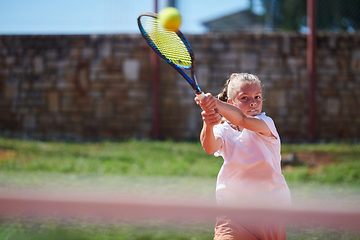 Image showing A young girl showing professional tennis skills in a competitive match on a sunny day, surrounded by the modern aesthetics of a tennis court.