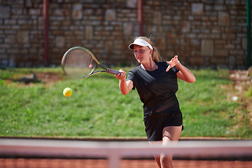 Image showing A young girl showing professional tennis skills in a competitive match on a sunny day, surrounded by the modern aesthetics of a tennis court.