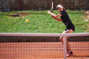 Image showing A young girl showing professional tennis skills in a competitive match on a sunny day, surrounded by the modern aesthetics of a tennis court.