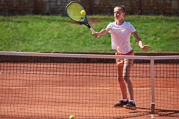 Image showing A young girl showing professional tennis skills in a competitive match on a sunny day, surrounded by the modern aesthetics of a tennis court.