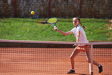 Image showing A young girl showing professional tennis skills in a competitive match on a sunny day, surrounded by the modern aesthetics of a tennis court.