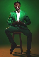 Image showing Fashion, trendy and black man model in a suit on chair in the studio with elegant, fancy and stylish outfit. Happy, smile and portrait of African male with formal clothes isolated by green background