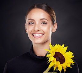 Image showing Skincare, beauty and portrait of a woman with a sunflower in a studio for a clean, healthy and organic routine. Cosmetic, floral and model from Brazil with natural face treatment by black background.