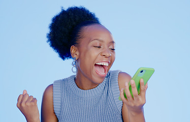 Image showing Celebration. phone and young black woman in a studio with winning, achievement or success. Happy, smile and African female winner cheering with fist pump on cellphone isolated by blue background.