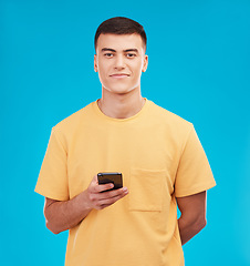 Image showing Phone, portrait and young man in studio networking on social media, mobile app or internet. Smile, technology and male person from Canada scroll on website with cellphone isolated by blue background.