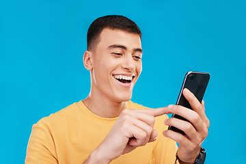 Image showing Phone, excited and young man in a studio scroll on social media, mobile app or the internet. Smile, happy and male person from Canada networking on website with cellphone isolated by blue background.
