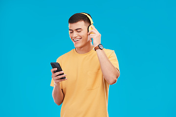 Image showing Phone headphones and young man in a studio listening to music, radio or playlist for entertainment. Smile, technology and male person streaming a song, podcast or album isolated by blue background.