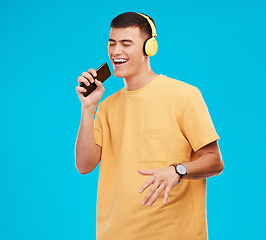 Image showing Phone, headphones and man singing in studio listening to music, radio or playlist for entertainment. Smile, technology and male person streaming song or album for karaoke isolated by blue background.