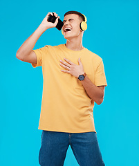 Image showing Phone, headphones and man singing in studio listening to music, radio or playlist for entertainment. Smile, technology and male person streaming song or album for karaoke isolated by blue background.