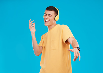 Image showing Dance, headphones and young man in a studio listening to music, radio or playlist for entertainment. Smile, technology and male person moving and streaming a song or album isolated by blue background