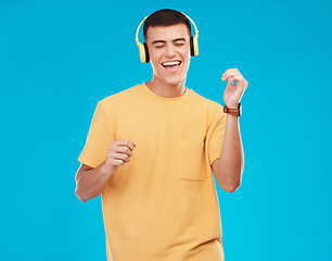 Image showing Dancing, headphones and young man in a studio listening to music, radio or playlist for entertainment. Smile, technology and male person moving and streaming song or album isolated by blue background