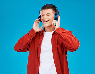 Image showing Man, smile and headphones for streaming radio in studio by blue background. Asian person, listening and chilling to song, radio and audio or hearing a funny podcast, technology and sound for joy