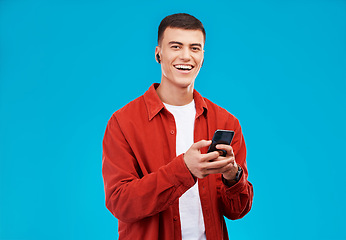 Image showing Man, phone and listening to music in studio with social media, college contact and communication on a blue background. Portrait of person or student in USA with mobile, earphones or audio streaming
