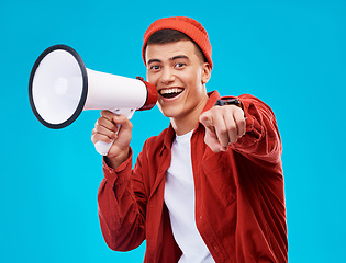 Image showing Portrait, bullhorn and young man in studio pointing for an announcement or speech at a rally. Happy, smile and male activist on stool with megaphone for loud communication isolated by blue background