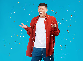 Image showing Portrait, confetti and man with celebration, achievement and excited on a blue background. Person, guy and model with sparkle, success and happiness with surprise, wow and omg with victory or winning