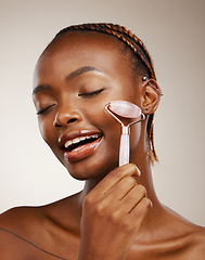 Image showing Woman, face roller and massage in studio for skincare, rose quartz cosmetics and aesthetic dermatology on brown background. African model, crystal stone tools and lymphatic drainage for facial beauty