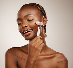 Image showing Happy woman, face roller and massage for beauty, rose quartz cosmetics and aesthetic dermatology in studio on brown background. African model, crystal stone and lymphatic drainage for facial skincare